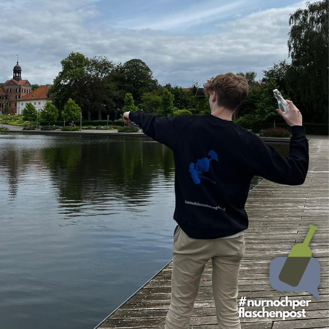 Ein Schülervertreter, der die Flaschenpost in der Hand hält. Am unteren rechten Rand steht: #nurnochperflaschenpost