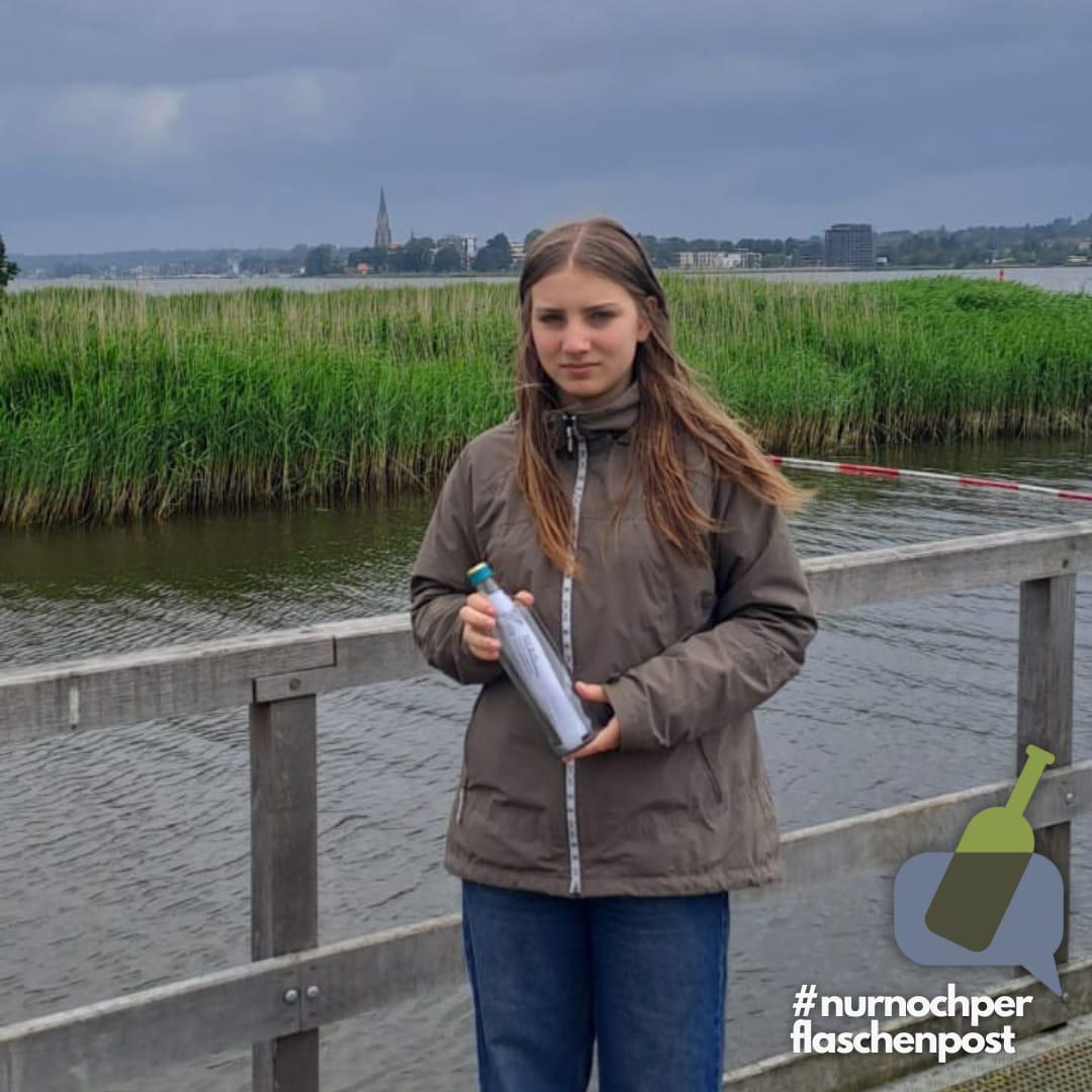 Eine Schülervertreterin, hält die Flaschenpost in der Hand. Am unteren rechten Rand steht: #nurnochperflaschenpost